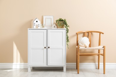 Photo of Dresser with stylish decor and houseplant near beige wall indoors