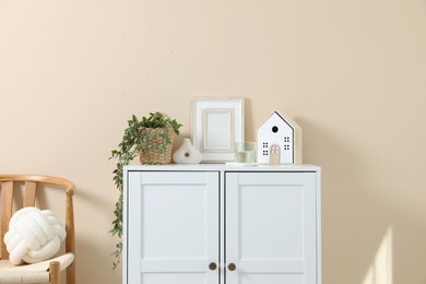 Photo of Dresser with stylish decor and houseplant near beige wall indoors