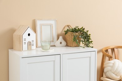Photo of Dresser with stylish decor and houseplant near beige wall indoors