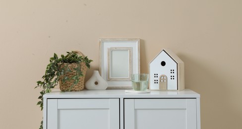 Photo of Dresser with stylish decor and houseplant near beige wall indoors