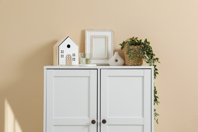 Photo of Dresser with stylish decor and houseplant near beige wall indoors