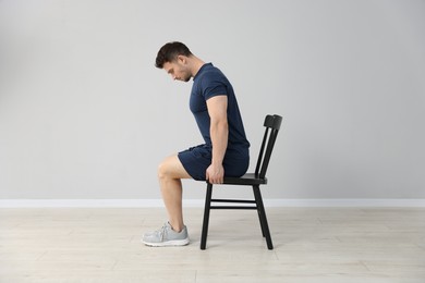 Photo of Handsome man exercising with chair at home