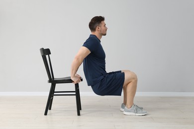 Photo of Handsome man exercising with chair at home