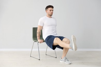 Photo of Handsome man exercising with chair at home