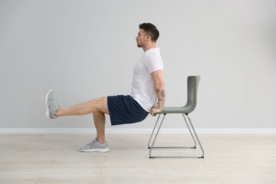 Photo of Handsome man exercising with chair at home