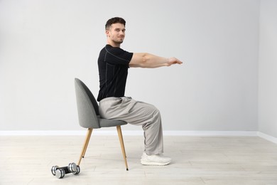 Photo of Handsome man exercising with chair at home