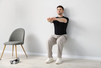 Photo of Handsome man exercising near light grey wall indoors