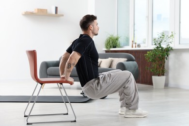 Photo of Handsome man exercising with chair at home