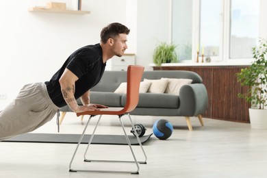 Photo of Handsome man exercising with chair at home