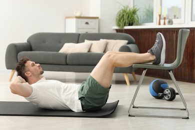 Photo of Handsome man exercising with chair at home