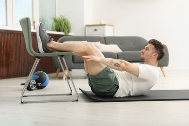 Photo of Handsome man exercising with chair at home