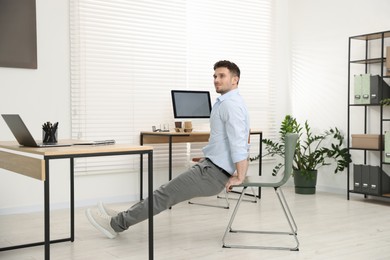 Photo of Handsome man exercising with chair in office