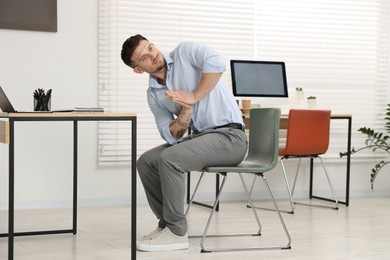 Photo of Handsome man exercising with chair in office
