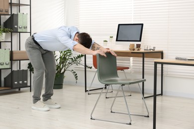 Photo of Young man exercising with chair in office