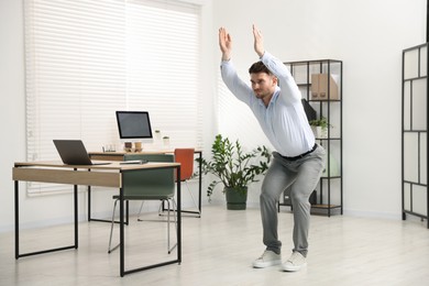 Photo of Handsome man doing exercise near desk in office