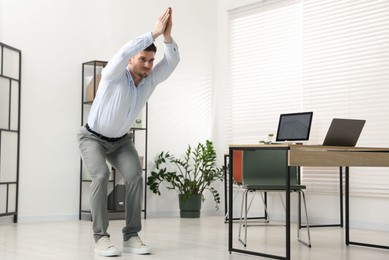 Photo of Handsome man doing exercise near desk in office