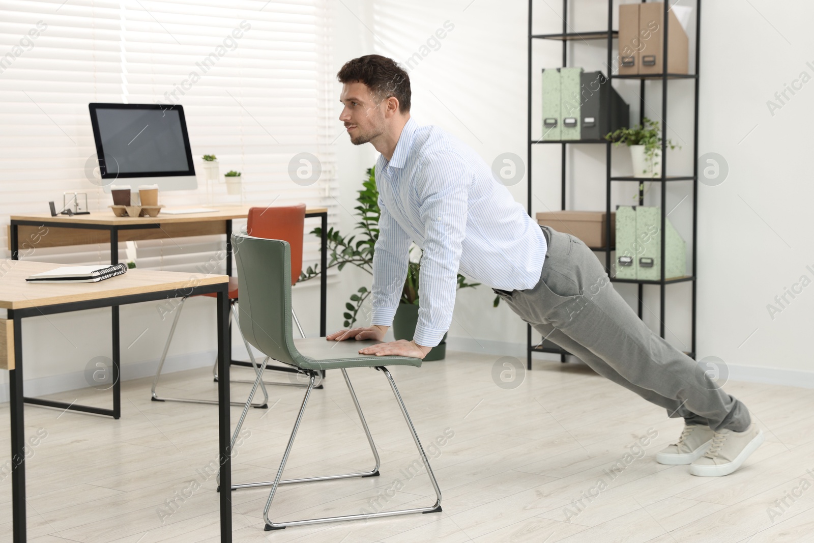 Handsome man exercising with chair in office Photo of Handsome man exercising with chair in office