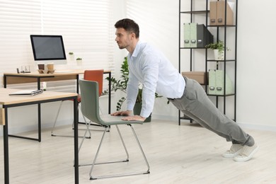 Photo of Handsome man exercising with chair in office
