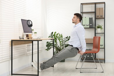 Photo of Handsome man exercising with chair in office