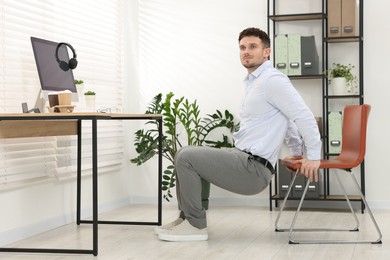 Photo of Handsome man exercising with chair in office