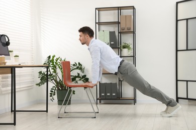 Photo of Handsome man exercising with chair in office