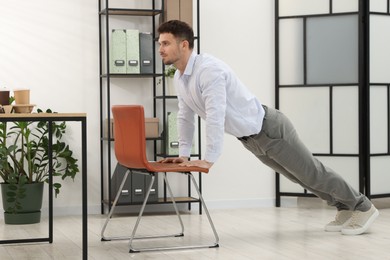 Photo of Handsome man exercising with chair in office