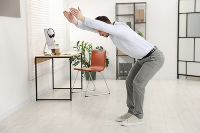 Photo of Handsome man doing exercise near desk in office