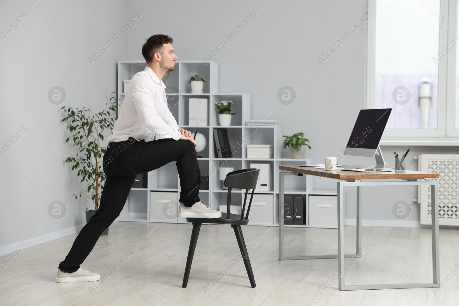 Handsome man exercising with chair in office Photo of Handsome man exercising with chair in office