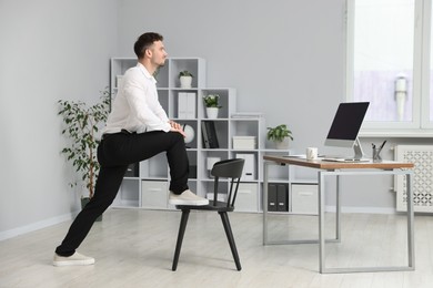 Photo of Handsome man exercising with chair in office