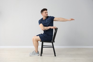 Photo of Handsome man exercising with chair at home
