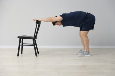 Photo of Handsome man exercising with chair at home