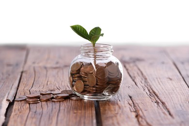 Photo of Investment concept. Glass jar with coins and sprout on wooden table against light background