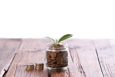 Photo of Investment concept. Glass jar with coins and sprout on wooden table against light background