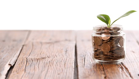 Photo of Investment concept. Glass jar with coins and sprout on wooden table against light background, space for text