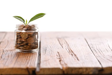 Photo of Investment concept. Glass jar with coins and sprout on wooden table against light background, space for text
