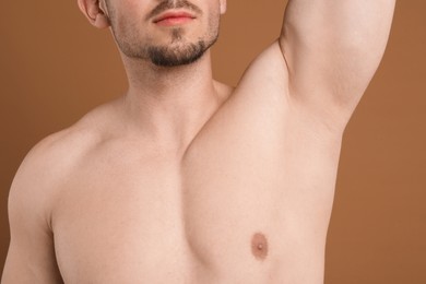 Photo of Young man showing smooth armpit after epilation procedure on brown background