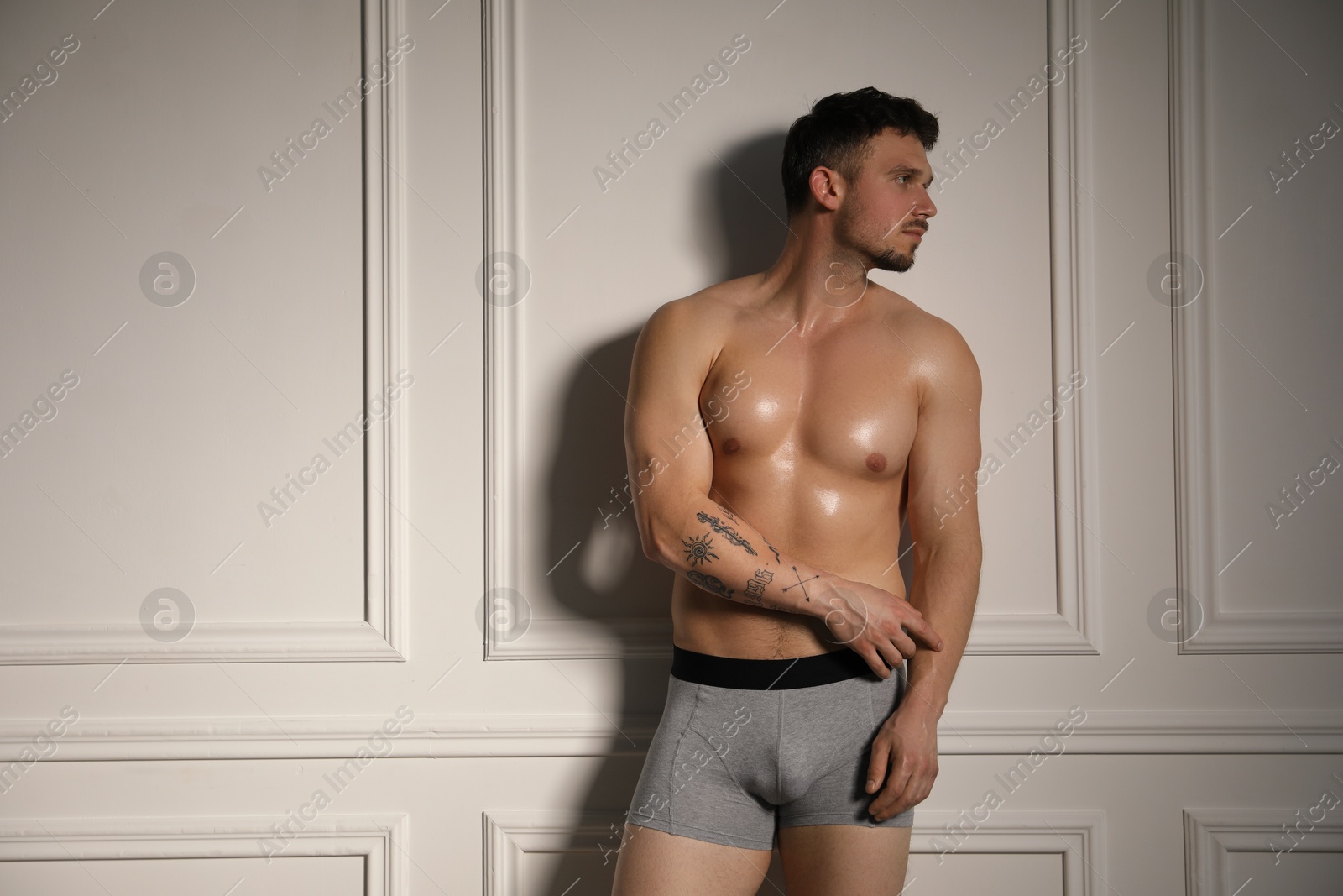 Young man in stylish light grey underwear near white wall indoors Photo of Young man in stylish light grey underwear near white wall indoors