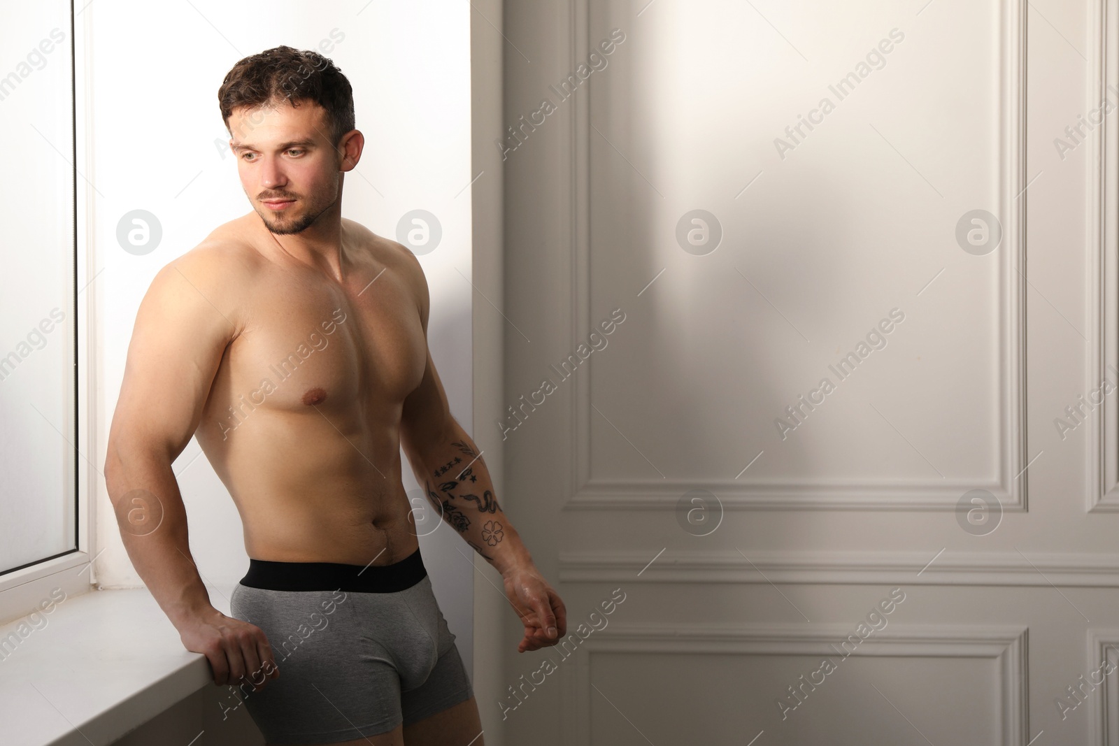 Young man in stylish light grey underwear near white wall indoors. Space for text Photo of Young man in stylish light grey underwear near white wall indoors. Space for text