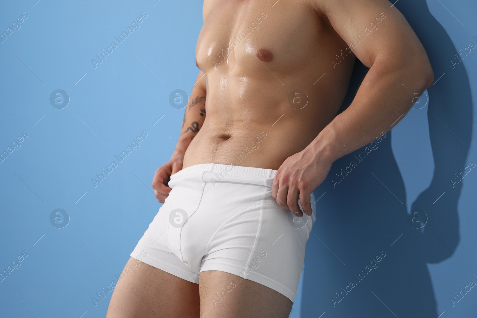 Young man in stylish white underwear near light blue wall indoors, closeup Photo of Young man in stylish white underwear near light blue wall indoors, closeup