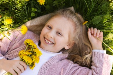 Photo of Cute little girl with beautiful dandelions on green grass outdoors, top view