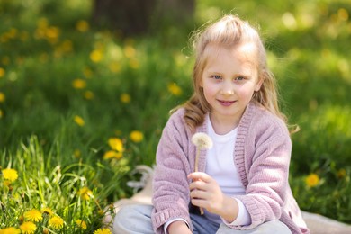 Photo of Cute little girl with beautiful dandelion on green grass outdoors, space for text