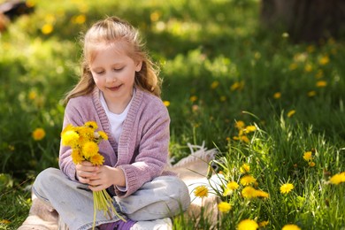Photo of Cute little girl with beautiful dandelions on green grass outdoors, space for text