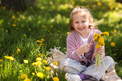 Photo of Cute little girl with beautiful dandelions on green grass outdoors, space for text