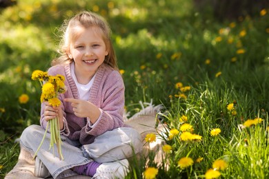 Photo of Cute little girl with beautiful dandelions on green grass outdoors, space for text