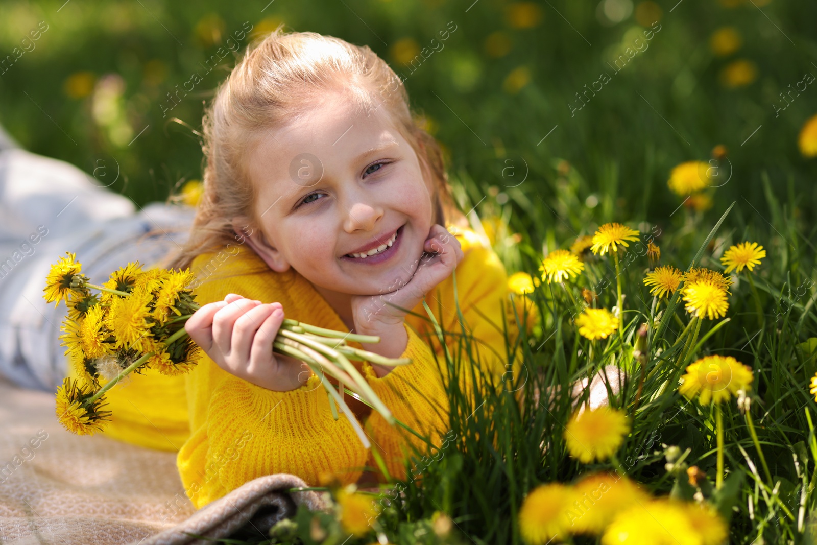 Cute little girl with beautiful dandelions on green grass outdoors Photo of Cute little girl with beautiful dandelions on green grass outdoors