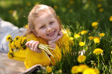 Photo of Cute little girl with beautiful dandelions on green grass outdoors