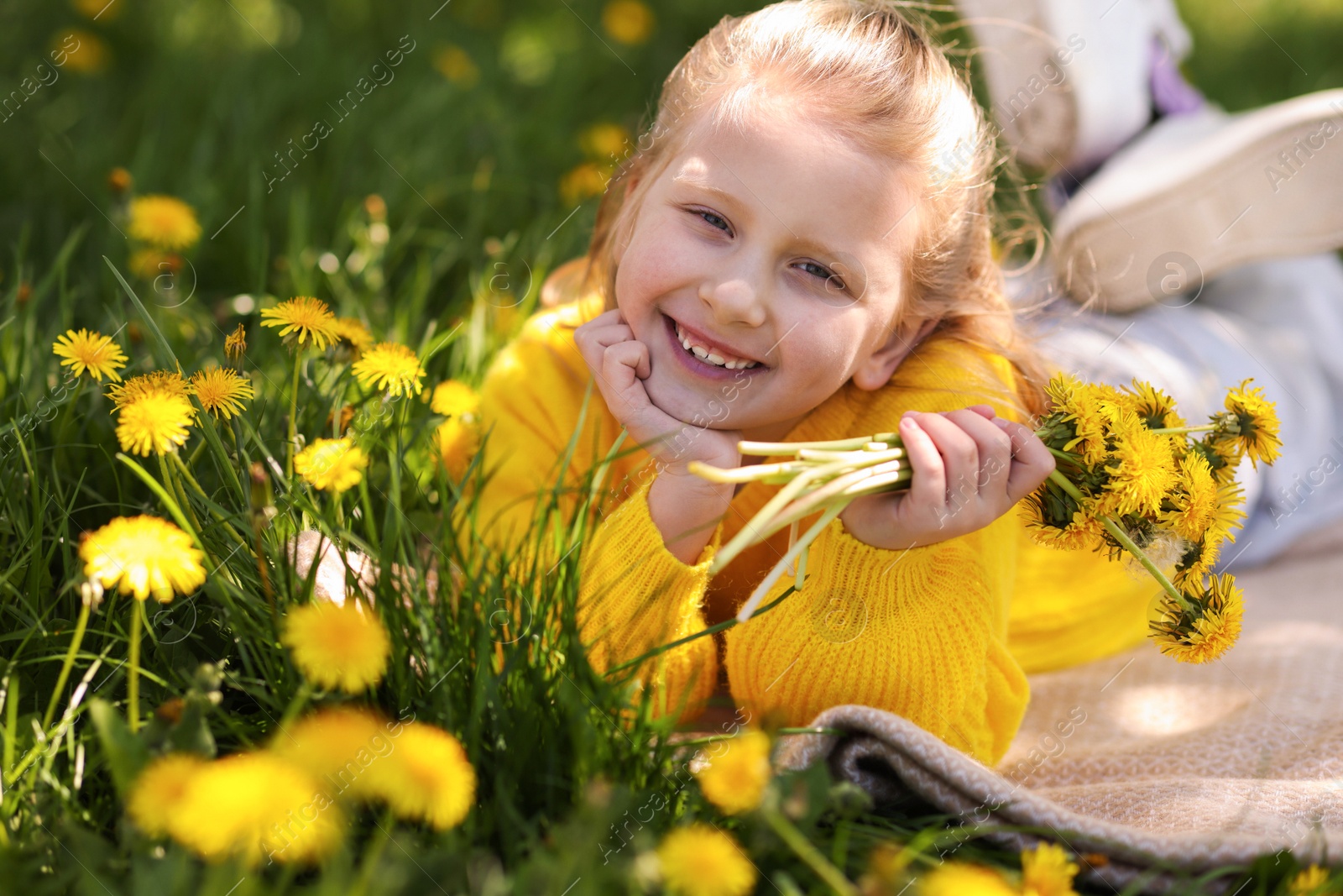 Cute little girl with beautiful dandelions on green grass outdoors Photo of Cute little girl with beautiful dandelions on green grass outdoors