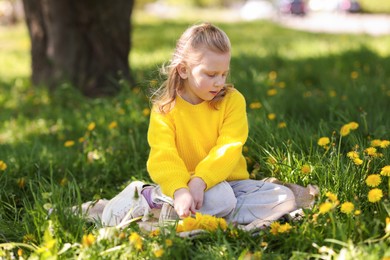 Photo of Cute little girl picking beautiful dandelions in park