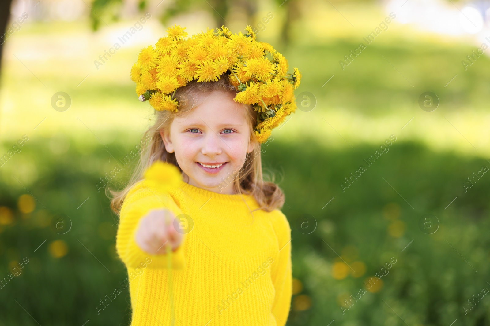 Cute little girl with beautiful flower wearing wreath of dandelions in park Photo of Cute little girl with beautiful flower wearing wreath of dandelions in park