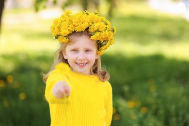 Photo of Cute little girl with beautiful flower wearing wreath of dandelions in park
